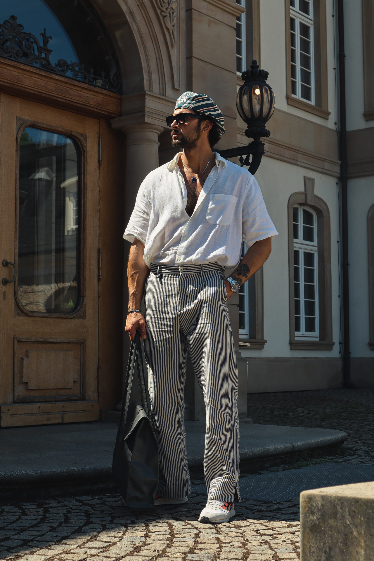 Full-length photo of Anil in a white linen shirt and striped trousers outside a historic building