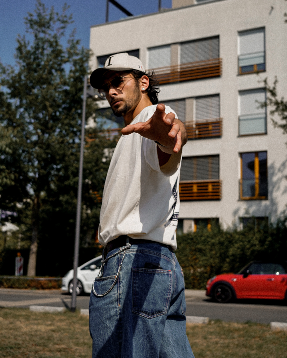 Anil in an oversized white tee and wide denim jeans reaching toward the camera