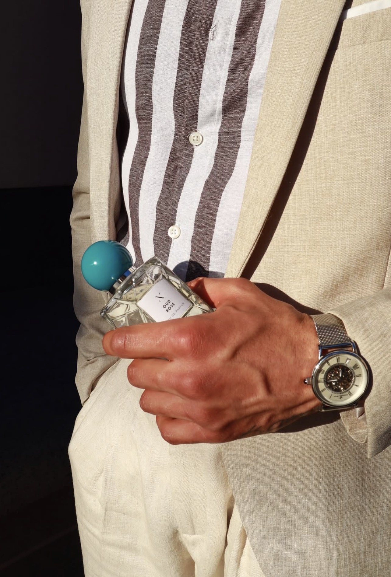 Close-up of Anil in a cream linen suit holding an Oud Rose eau de parfum bottle